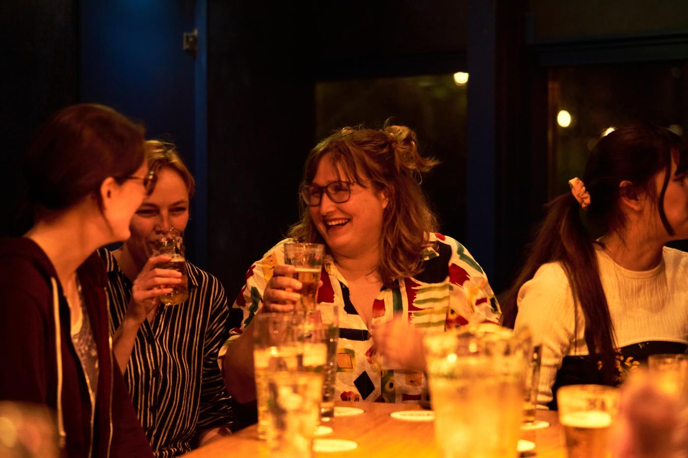 Vier studenten zitten aan de bar met drankjes voor hun op tafel en biertjes in hun hand. Ze lachen en hebben plezier.