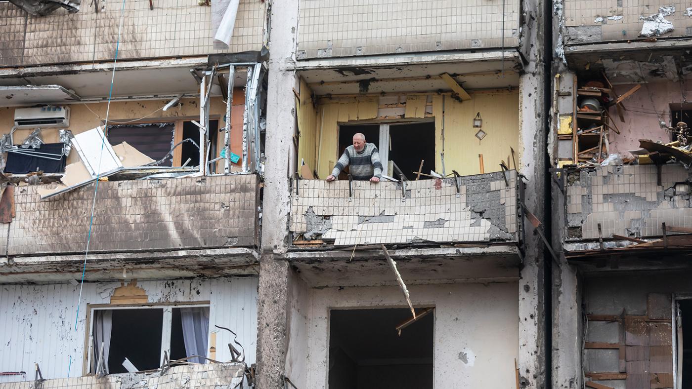 A man looks out the window of a residential building damaged by air strikes in Kyiv, Ukraine. Photo: Shutterstock, February 2022. A man looks out the window of a residential building damaged by air strikes in Kyiv, Ukraine.