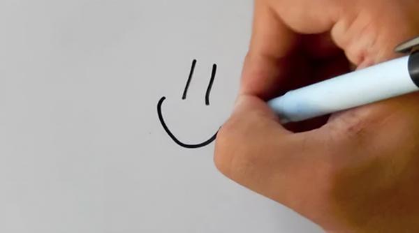 A hand holding a marker and drawing a smiley face