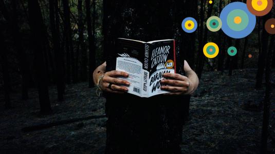 Een donkere afbeelding met in het midden een tijdens de bosbranden in noordwest Spanje verbrande boom. Van achter de boom komen twee armen die het boek 'Birnam Wood' opgeslagen vasthebben.